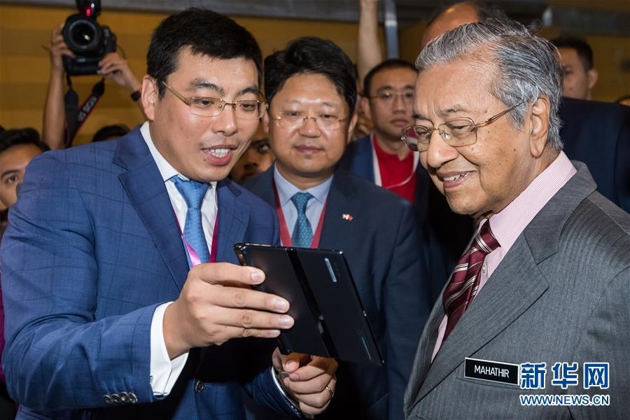 4月18日，在马来西亚普特拉贾亚，马来西亚总理马哈蒂尔（右）在5G技术展上听取华为5G智能手机的介绍。 由马来西亚通信与多媒体部主办的马来西亚5G技术展18日在该国行政首都普特拉贾亚开幕，会上展出了5G通信和应用技术，华为等中国企业参展。 新华社记者 朱炜 摄